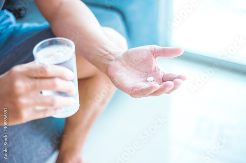 One round white pill in hand. Man takes medicines with glass of water. Daily norm of vitamins, effective drugs, modern pharmacy for body and mental health.