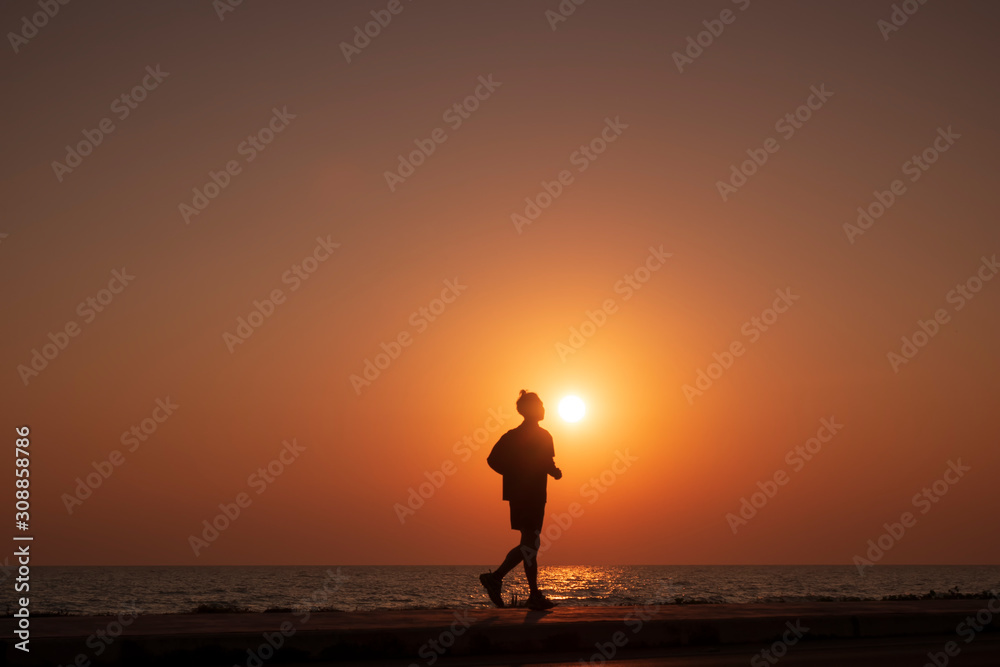 Silhouette of man jogging for exercise on beach at sunrise