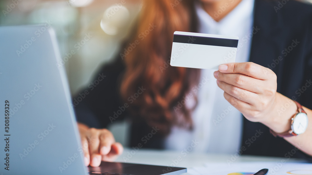 An asian businesswoman holding credit cards while using laptop computer in office