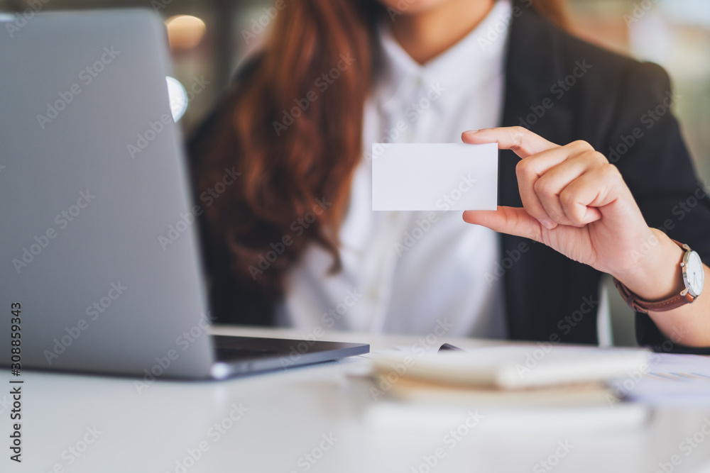 A businesswoman holding and showing a blank business cards while using laptop computer in office A businesswoman holding and showing a blank business cards while using laptop computer in office