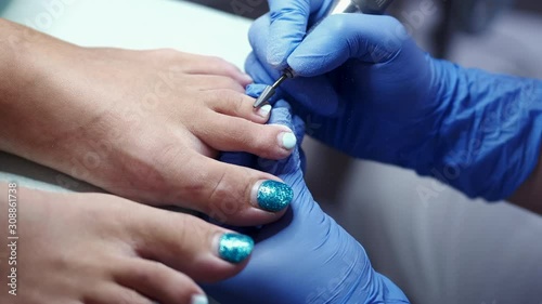 The pedicure technician is polishing nails in a beauty salon. She is performing with the help of a milling cutter. photo