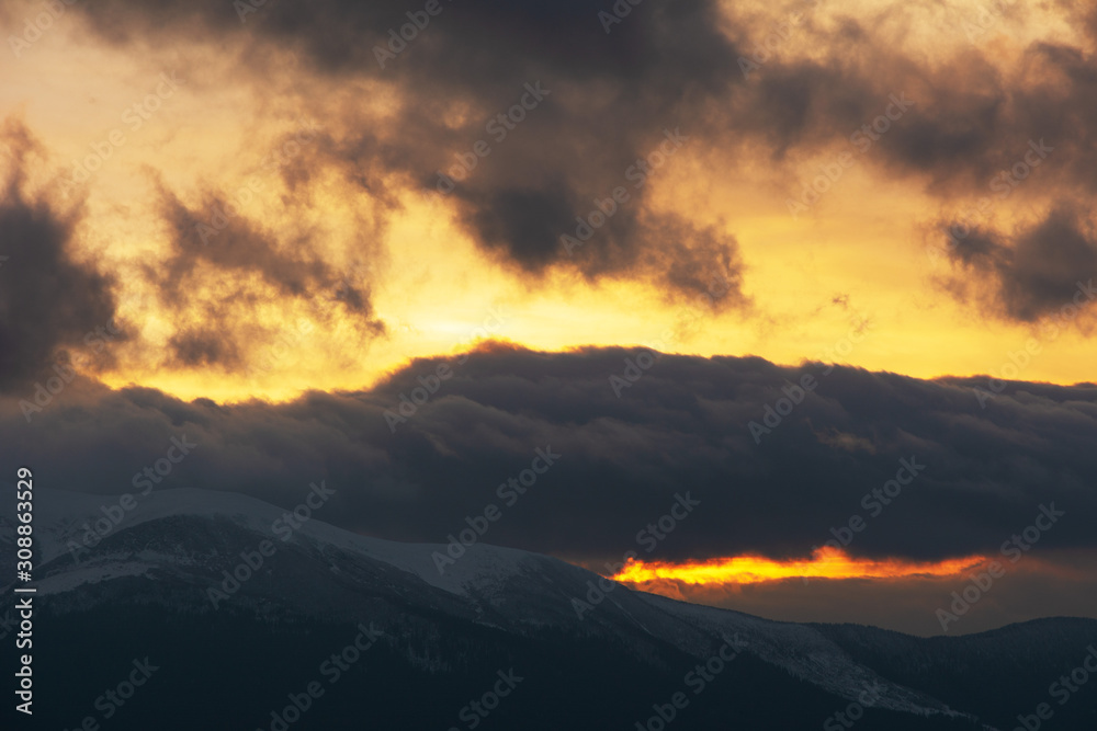 Evening dramatic sky with colorful burning clouds against the backdrop of mountain houses in winter