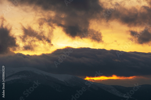 Evening dramatic sky with colorful burning clouds against the backdrop of mountain houses in winter