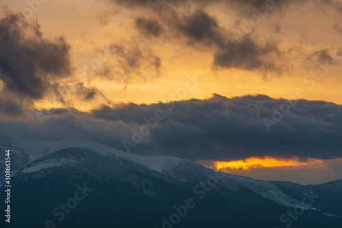 Evening dramatic sky with colorful burning clouds against the backdrop of mountain houses in winter