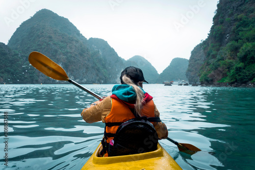 Vászonkép Young beautiful woman floating on a kayak between the rocks sticking out of the sea
