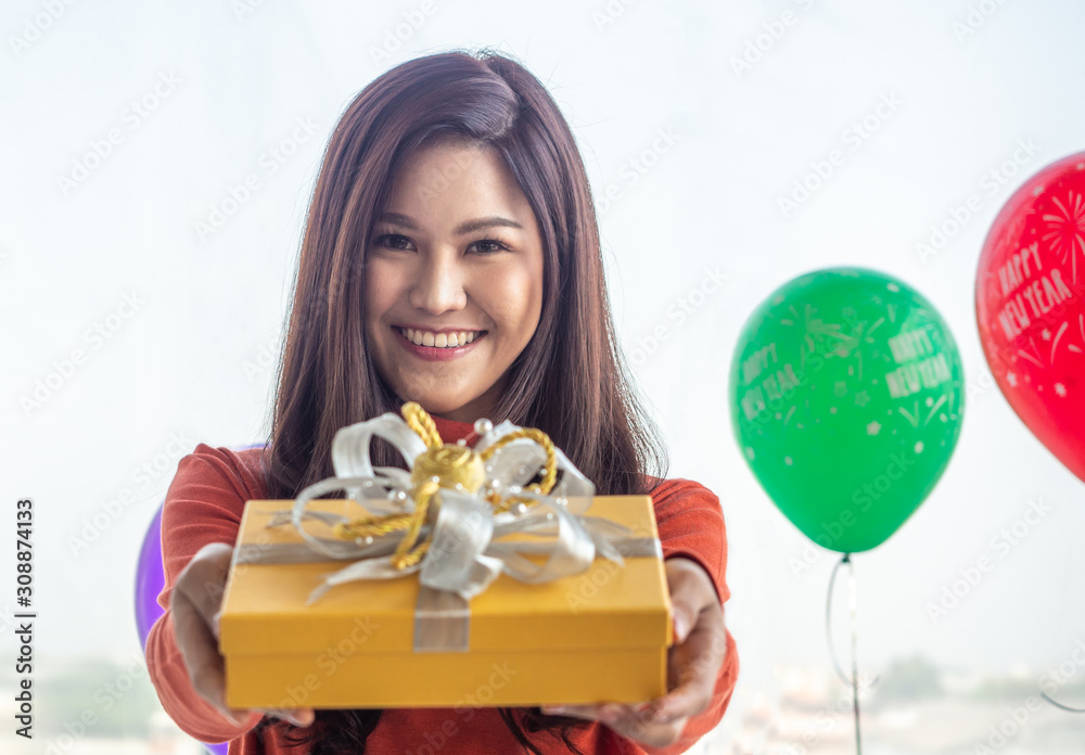 A beautiful, long-haired Asian woman wearing a red sweater smiled joyfully for the camera at the New Year's Eve celebration and Christmas. She held a yellow gift box in her hand. A beautiful, long-haired Asian woman wearing a red sweater smiled joyfully for the camera at the New Year's Eve celebration and Christmas. She held a yellow gift box in her hand.