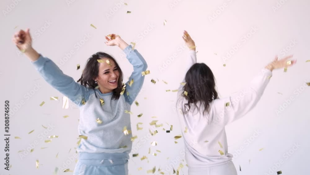 Attractive girls dancing and having fun throwing confetti on a white background. Brunette women celebrate, portray joy and happiness. Success, party, celebration concept. Attractive girls dancing and having fun throwing confetti on a white background. Brunette women celebrate, portray joy and happiness. Success, party, celebration concept.