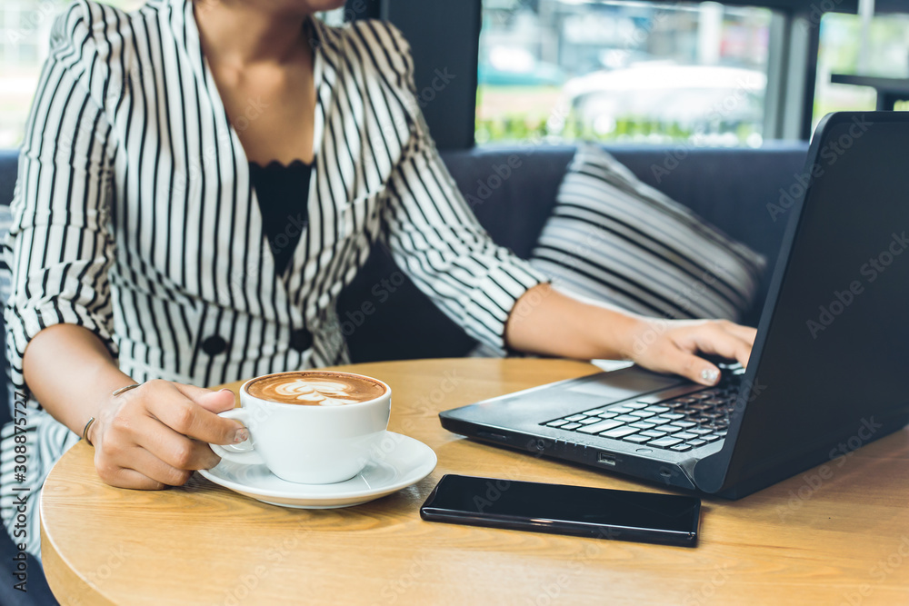 businesswomen working with laptop and hand catch cup of coffee. A mobile phone is on the table near the laptop. businesswomen working with laptop and hand catch cup of coffee. A mobile phone is on the table near the laptop.