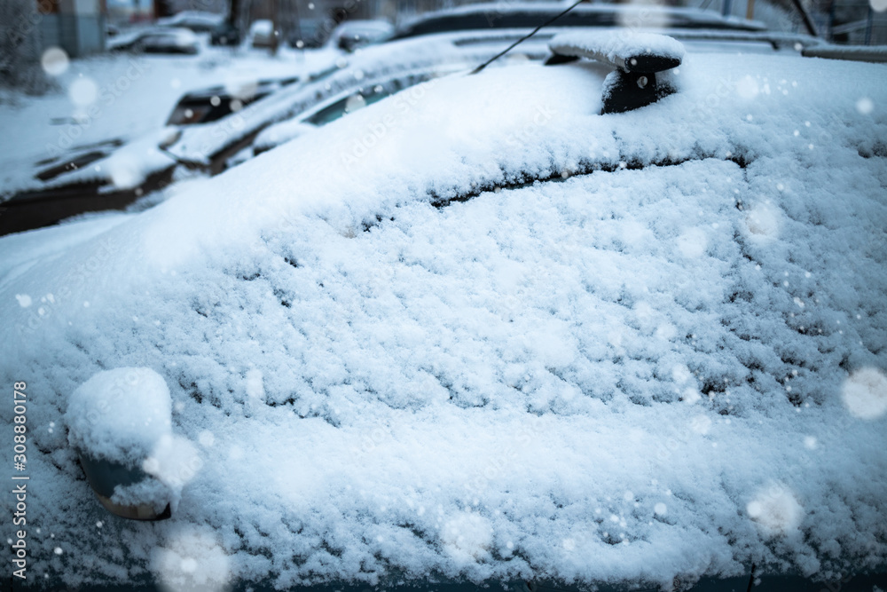 The car is covered in snow. In the frame, the side. Snow falls. Glass in focus blurred background.