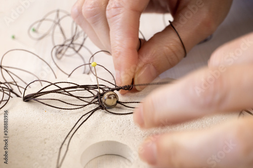 Lifestyle concept, reinvent your life and your job: close-up detail of woman hands making macrame knotted jewel with the fingers that tie the nylon thread around the diaspro natural stone photo