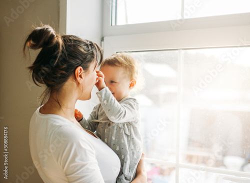 Young woman mom with baby girl on hands near window at home photo