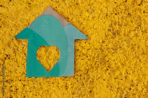 Casa de papel verde  ,con fondo amarillo, sujetado de una mano.