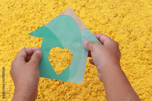 Casa de papel verde  ,con fondo amarillo, sujetado de una mano.