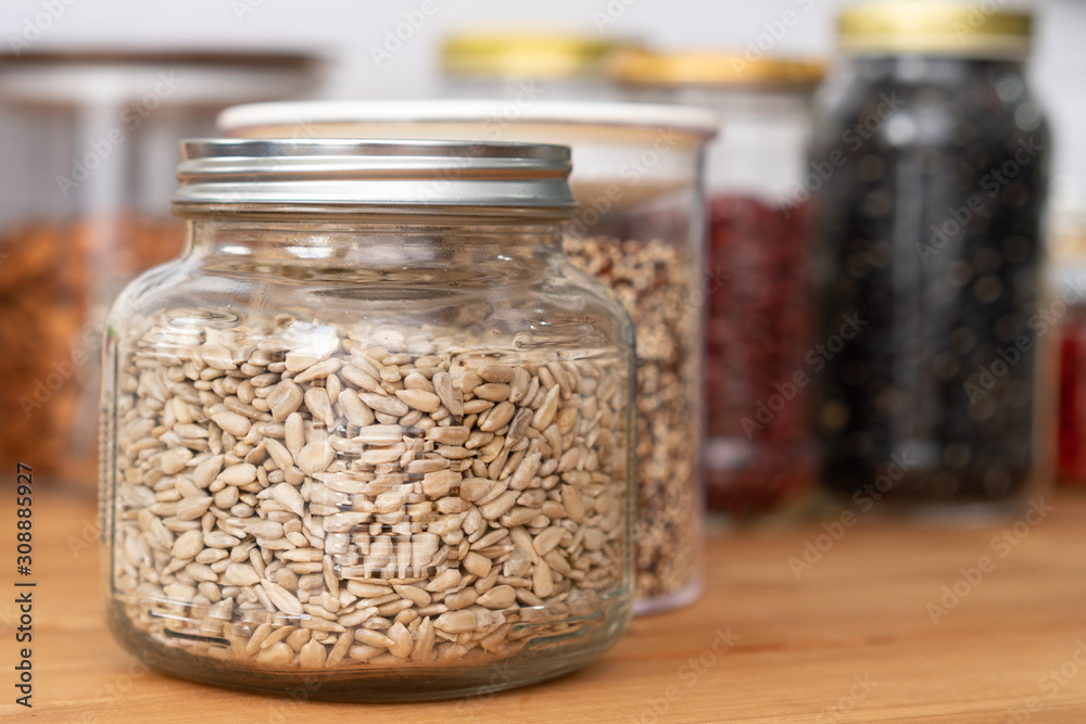 Closeup, Beautiful glass jar airtight container full of organic dried sunflower seeds on wooden kitchen table with other plant-based diet/vegan healthy nutrition source - beans, nuts, almonds, peas, g