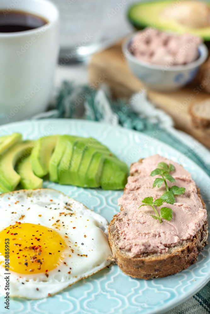 Healthy breakfast with cooked egg, chopped avocado on a plate, cereal bread with pate and herbs and a glass of water with coffee Healthy breakfast with cooked egg, chopped avocado on a plate, cereal bread with pate and herbs and a glass of water with coffee