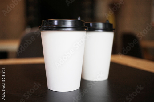 Several, two paper white cups with a plastic black lid for takeaway coffee on a black background of the table in the cafe.Close up view of disposable paper coffee Cup in cafe