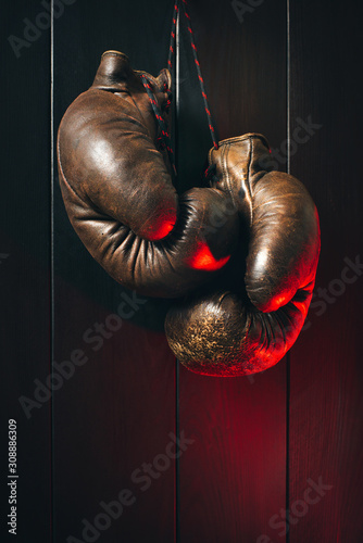 Boxing gloves, hanging on black wooden wall in red light. Copy space. © a_khachatryan