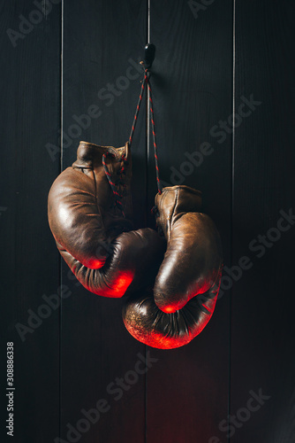 Old brown boxing gloves, hanging on black wooden wall in red lighting.  © a_khachatryan