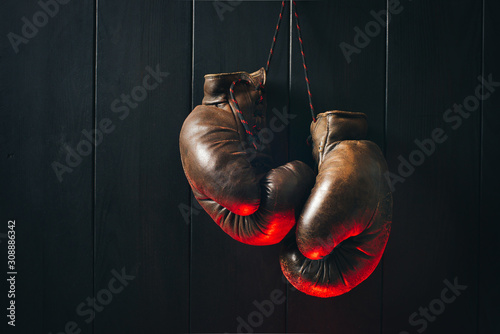Boxing gloves, hanging on black wooden wall in red light. Copy space. © a_khachatryan