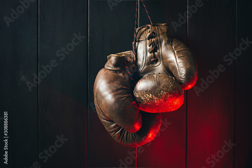 - Old brown boxing gloves, hanging on black wooden wall in dramatic red lighting. Copy space. © a_khachatryan