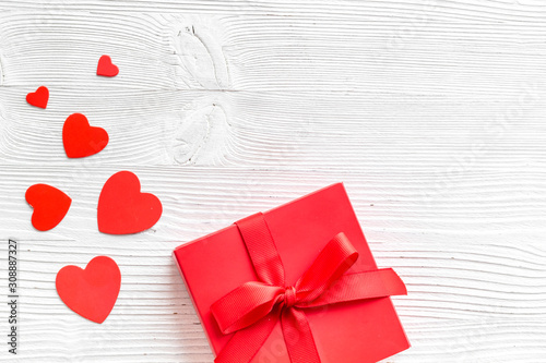 Gift to a sweetheart on Valentine's Day. Red present box near hearts on white wooden background top-down copy space