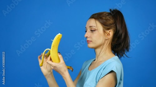 Pretty Brunette Young Woman Holding in Hand Yellow Banana and Then Eating it over Bright Blue Background. Tropical Fruits. Summer Concept. Healthy Eating. photo