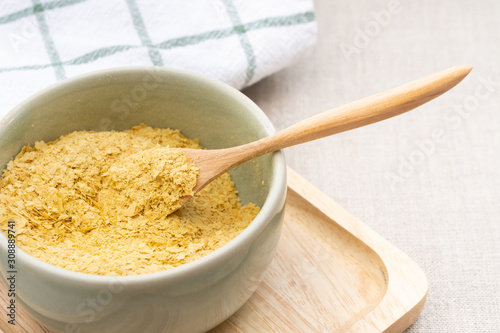 Top view & Closeup, Yellow flakes of nutritional yeast in ceramic bowl and wooden spoon, excellent source of vitamins, minerals, and high-quality protein for plant-based diet / vegan food.