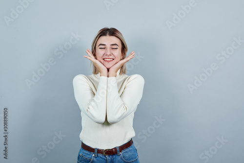 Portrait of charming girl teenager keeping hands near face isolated on gray wall background in studio. People sincere emotions, lifestyle concept.