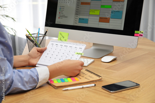Woman making schedule using calendar at table in office, closeup photo