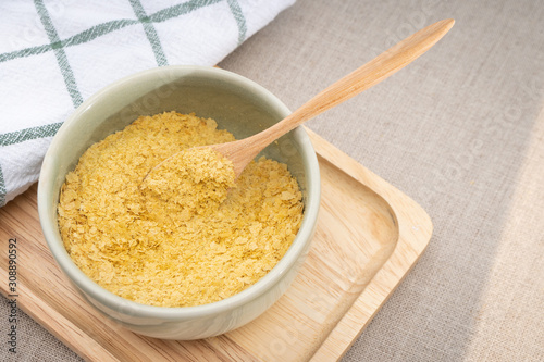 Top view & Closeup, Yellow flakes of nutritional yeast in ceramic bowl and wooden spoon, excellent source of vitamins, minerals, and high-quality protein for plant-based diet / vegan food. photo