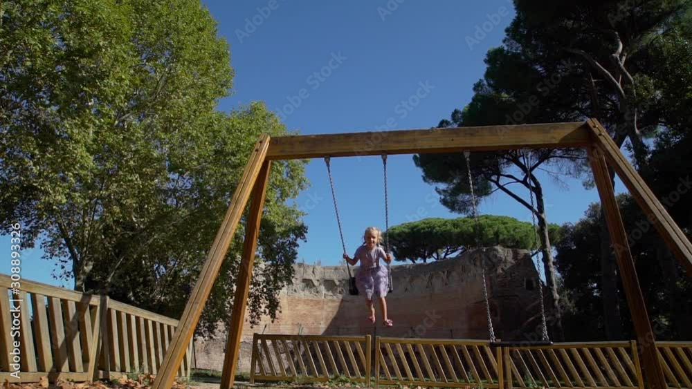 Cute Little Girl in Violet Dress Swinging in a City Park near Ancient Roman Building in Rome, Italy. Family Holidays, Vacation and People Concept Cute Little Girl in Violet Dress Swinging in a City Park near Ancient Roman Building in Rome, Italy. Family Holidays, Vacation and People Concept