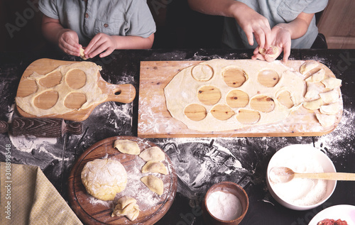   Little kids - boys, brothers making dumplings or ravioli, preparing dough in the kitchen with hands, wooden boards, flour. Child cooking concept. 