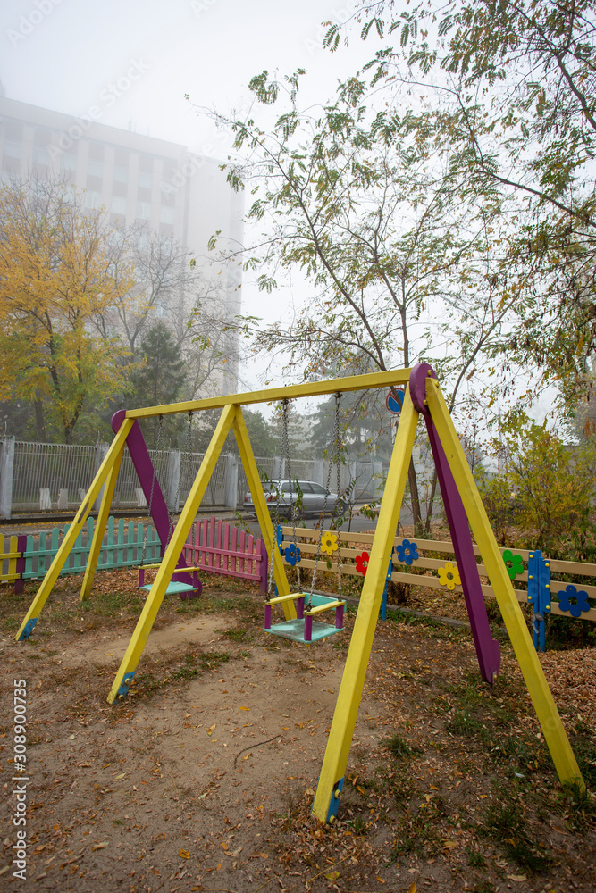Fototapeta premium Pair of colorful swings abandoned in a foggy playground