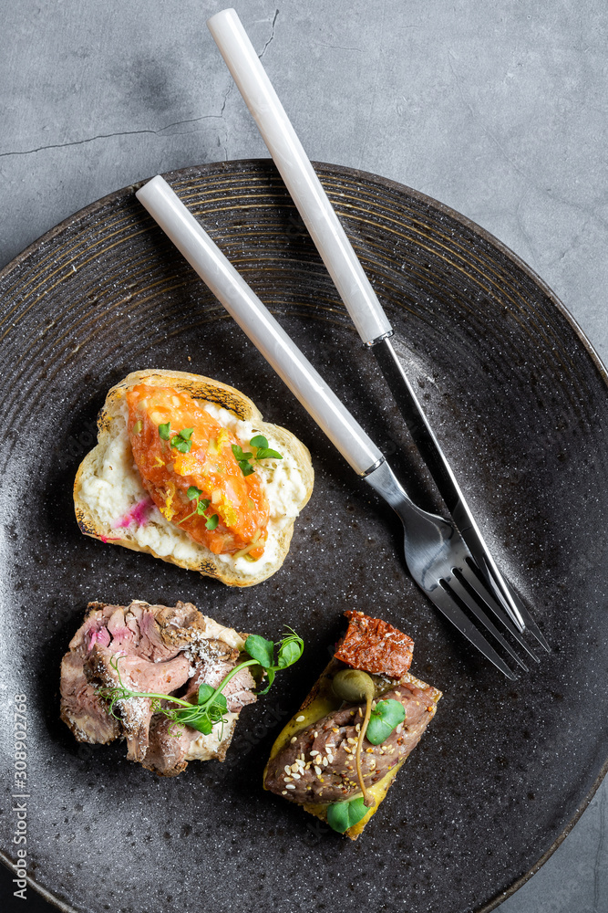 Three tapas sandwiches on a dark dish on a dark concrete table. Tasty snacks. Three tapas sandwiches on a dark dish on a dark concrete table. Tasty snacks.