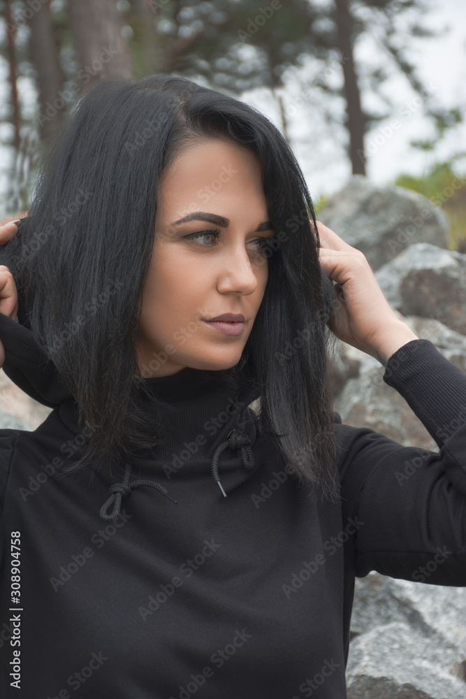 Close up portrait of attractive young brunette woman with black hair in black hooded sweatshirt outdoor. Magic sight, power of sight.