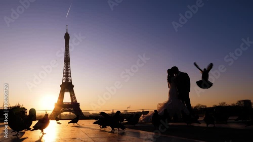Silhouette of kissing newlyweds on a eiffel tower background. Sunrise and pigeons around. Paris