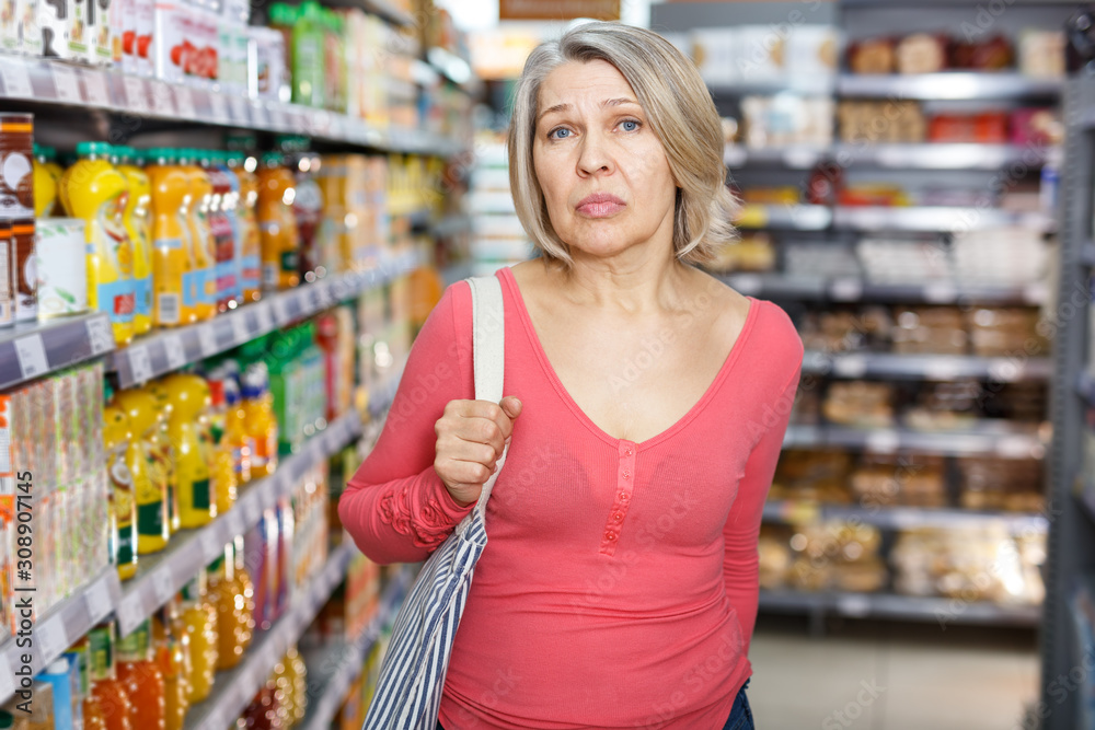 Thoughtful mature woman among shelves in grocery shop
