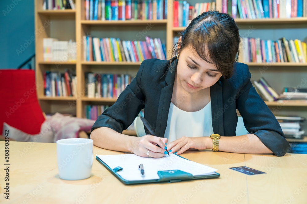 woman writing her working sheet in her university library, academic education concept