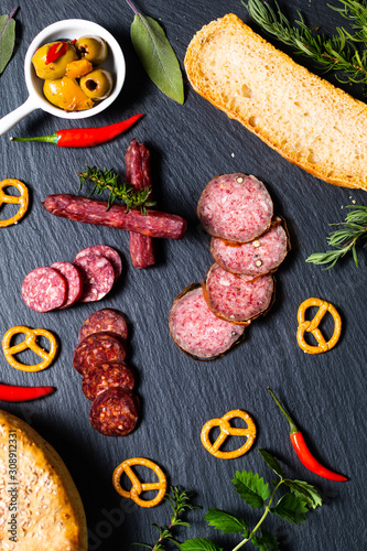 Food party background 3kind of meat Saucisson french salami, olive, prezels and homemade bread on black slate stone