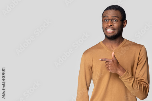 Obraz na plátně Worried african american guy, pointing aside at blank copy space.