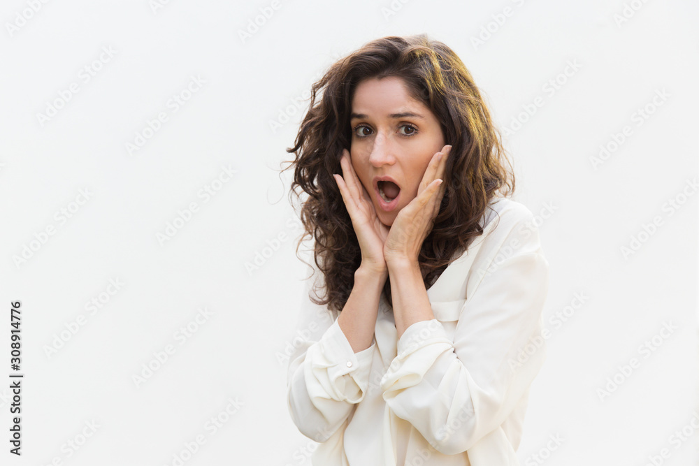 Worried excited woman gasping, touching face in surprise and staring at camera. Wavy haired young woman in casual shirt standing isolated over white background. Shocked customer concept Worried excited woman gasping, touching face in surprise and staring at camera. Wavy haired young woman in casual shirt standing isolated over white background. Shocked customer concept