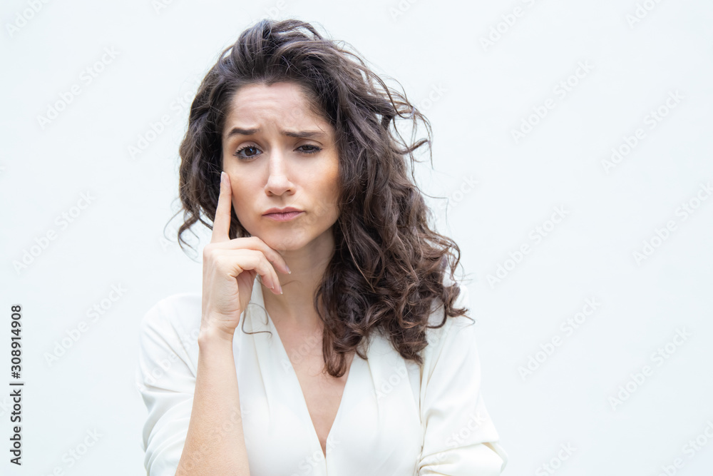 Pensive woman touching face with finger, looking at camera, thinking hard. Wavy haired young woman in casual shirt standing isolated over white background. Decision making concept Pensive woman touching face with finger, looking at camera, thinking hard. Wavy haired young woman in casual shirt standing isolated over white background. Decision making concept