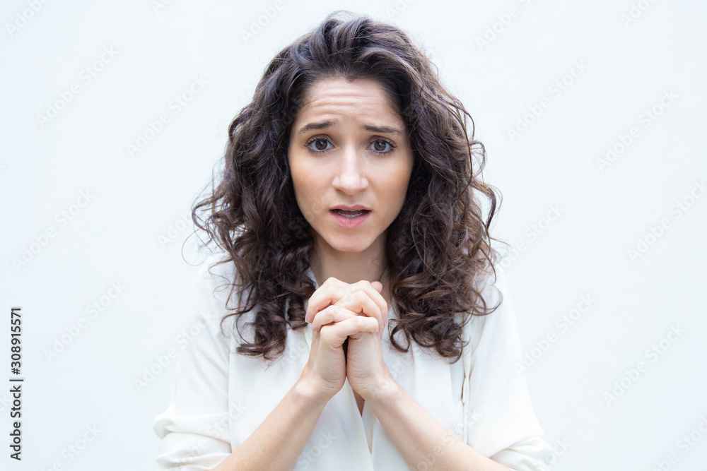 Cute worried student girl keeping hands in pray gesture. Wavy haired young woman in casual shirt standing isolated over white background. Prayer or asking for luck concept Cute worried student girl keeping hands in pray gesture. Wavy haired young woman in casual shirt standing isolated over white background. Prayer or asking for luck concept