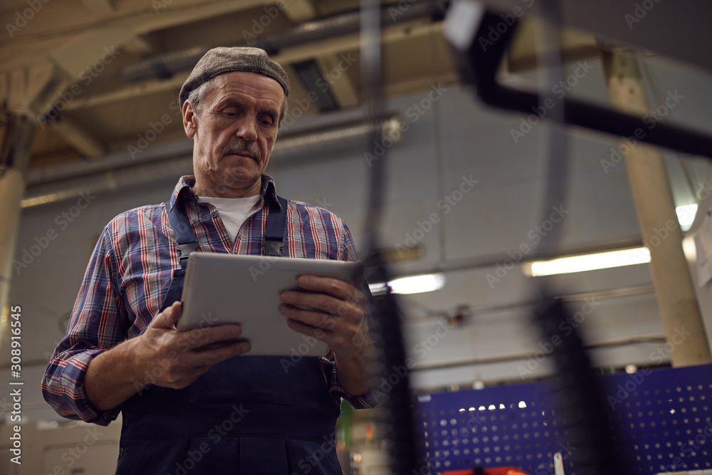 Senior operator using digital tablet and controlling the work of machine online in the factory Senior operator using digital tablet and controlling the work of machine online in the factory
