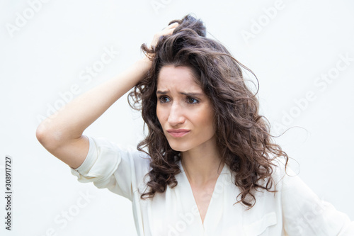 Stressed pensive desperate woman scratching head and looking away. Wavy haired young woman in casual shirt standing isolated over white background. Difficult decision concept