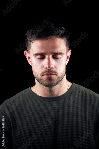 Studio Portrait Of Young Man With Serious Expression And Closed Eyes Against Black Background