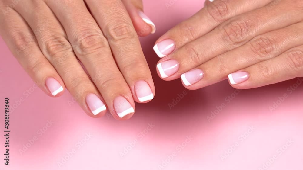Closeup top view of two beautiful female hands with classic white and pink french manicure at fingernails. Hands isolated on pastel pink background. Real time full hd video footage.