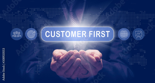 Obraz na płótnie Businessmans cupped hands holding a Customer First business concept on a computerised display. w salonie