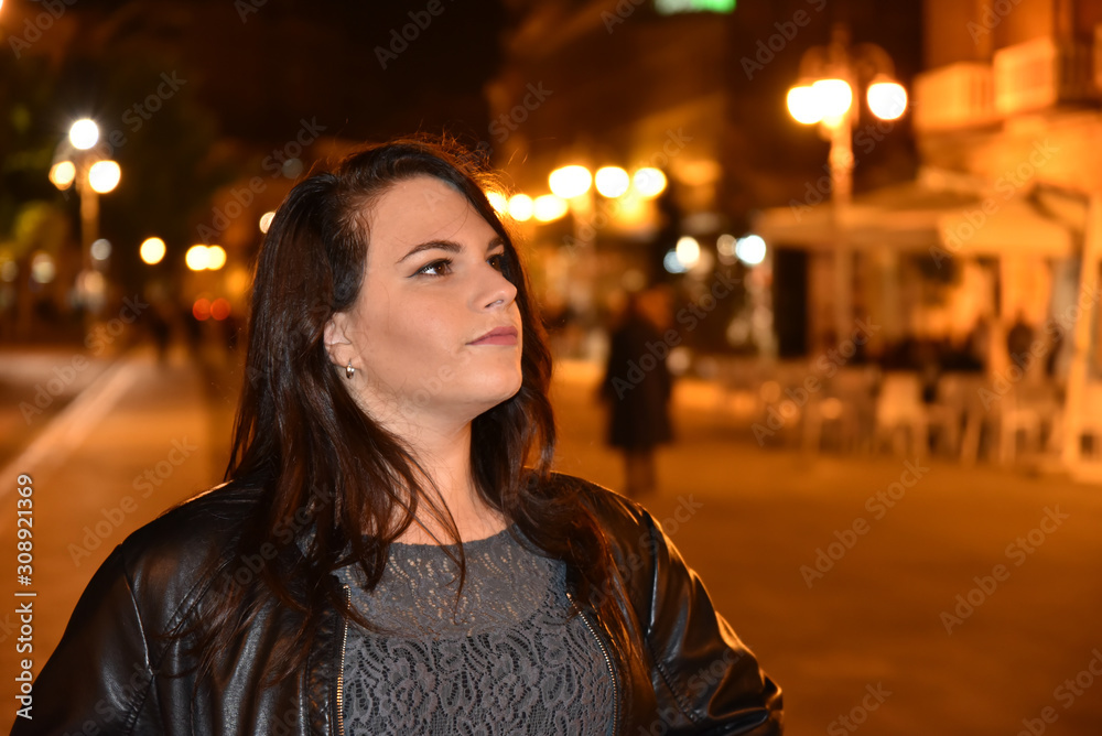 Night Portrait of Young Beautiful Woman in the City Illuminated by Lights Background