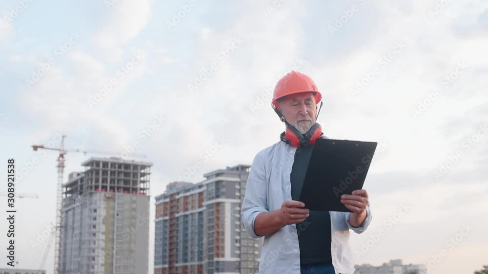 Engineer builder in constructor helmet with a gray beard on the background of construction Engineer builder in constructor helmet with a gray beard on the background of construction